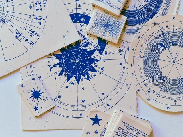 Flat lay of Synastral chart-wheel prints, star zines, and mini-reading cards in blue ink on cream paper